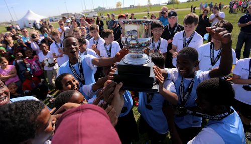 The players from IRCOM, The Immigrant and Refugee Community Organization of Manitoba Inc. soccer team, hoist their trophy as the players from St. Johns Ravenscourt look on, following the final game of the boys under 13 city recreation final at John Blumberg, Saturday, September 26, 2015. (TREVOR HAGAN/WINNIPEG FREE PRESS)