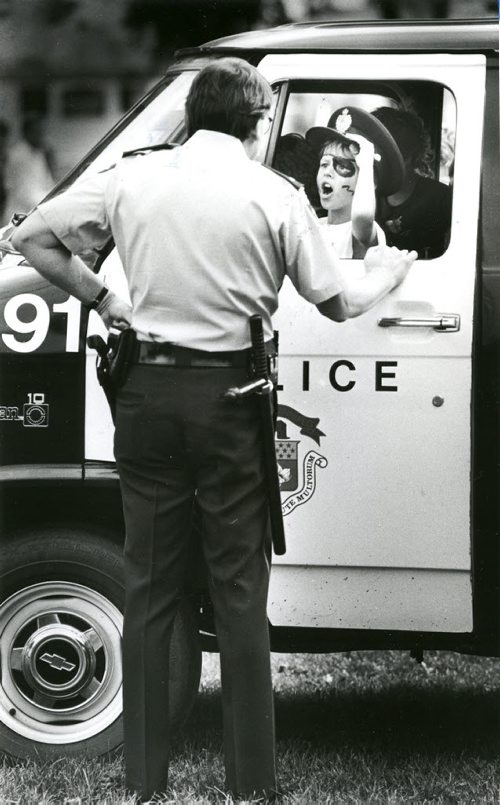 Const. John Campbell of the community relations unit appears to have lost his van and his cap to nine-year-old Leonard Mackie yesterday during Meet Your Neighbour Festival in Central Park. Leonard and his friends had been playing with the van's flashers and Campbell was trying to let him recharge the battery. August 9, 1986. Phil Hossack / Winnipeg Free Press