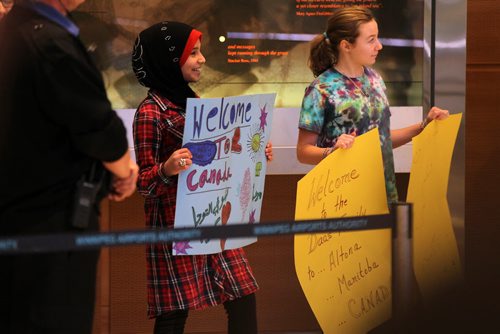 Twelve year old Wafaa Abukhousa (red) who was a refugee from Syria herself 6 years ago, holds a sign welcoming the new Syrian refugee families to Winnipeg at the airport Saturday.     See MA story.  Dec 19, 2015 Ruth Bonneville / Winnipeg Free Press
