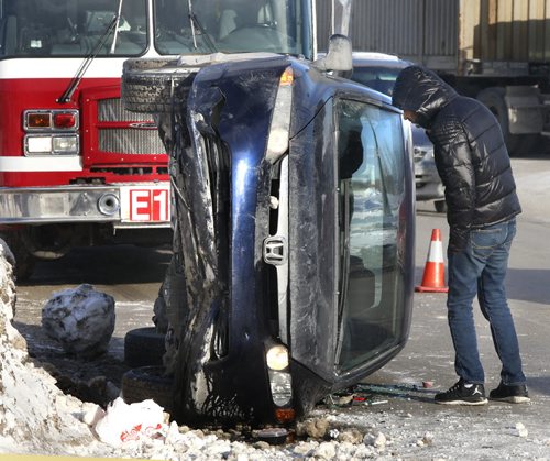 One of the two occupants in a car that overturned after hitting a snow bank in the 300 block of Keewatin St. Monday morning checks out the damage. No one was injured in the mishap. Wayne Glowacki / Winnipeg Free Press Jan. 18 2016