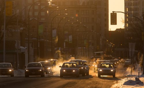 MIKE DEAL / WINNIPEG FREE PRESS The sun rises between downtown buildings as early morning traffic crawls along Notre Dame Avenue Tuesday morning. 160216 - Tuesday, February 16, 2016
