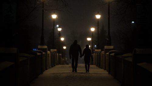 MIKE DEAL / WINNIPEG FREE PRESS A couple makes their way across the foot bridge in Assiniboine Park Wednesday evening as the snow continues to fall. 160316 - Wednesday, March 16, 2016