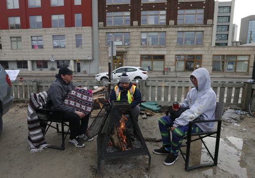 WAYNE GLOWACKI / WINNIPEG FREE PRESS  From left, protesters Ishkodai Bishiki, Animikii-Gekek and Stefan Vloknar by their sacred fire burning in a parking lot on Hargrave St. across from the Government of Canada's Aboriginal Affairs and Northern Development office Friday morning.  Protesters have been peacefully occupying the Winnipeg office for the past 24 hours in response to the suicide epidemic in Attiwaspikat and Pimicikamak. The protesters joined the #OccupyINAC campaign that originally began in Toronto on Wednesday.    April 15  2016