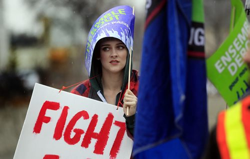 PHIL HOSSACK / WINNIPEG FREE PRESS Tiffani Sawatzky shelters under a flag supporting a $15 dollar an hour minimum wage Friday. Rallyer's gathered at the Univercity of Winnipeg Friday at noon before marching down Portage ave.  See story. APRIL 15, 2016