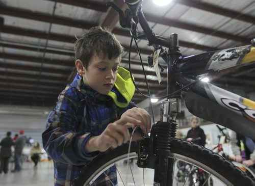 RUTH BONNEVILLE  Ten-year-old Hunter Wiebe, with the help of WRENCH volunteers, works on his new/used bike  that his mom bought for him at the City of Winnipeg annual unclaimed bike auction at East End Arena Saturday.Standup photo  April 16, 2016