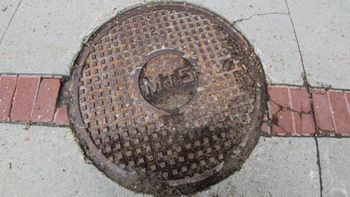 MIKE DEAL / WINNIPEG FREE PRESS An MTS manhole cover on the sidewalk outside the MTS building on Corydon Ave. 160526 - Thursday, May 26, 2016