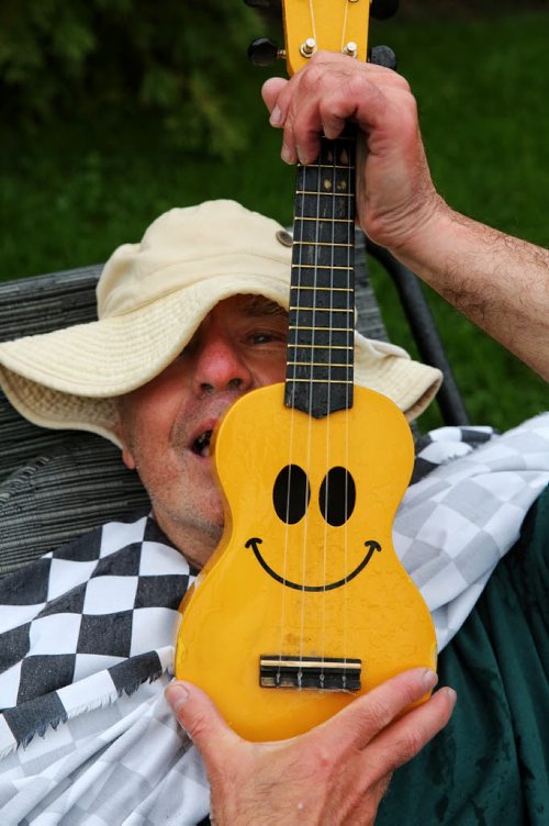 MIKE DEAL / WINNIPEG FREE PRESS  Winnipeg's Happy Dancer as he likes to call himself sitting on the front lawn of the Manitoba Legislative Building with his ukulele and a t-shirt that says "God Bless Taxes." He says he is retired and wanted be there despite the steady rain.   160531 Tuesday, May 31, 2016