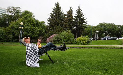 MIKE DEAL / WINNIPEG FREE PRESS  Winnipeg's Happy Dancer as he likes to call himself sitting on the front lawn of the Manitoba Legislative Building with his ukulele and a t-shirt that says "God Bless Taxes." He says he is retired and wanted be there despite the steady rain.   160531 Tuesday, May 31, 2016