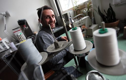 PHIL HOSSACK / WINNIPEG FREE PRESS -  THREADS -  Andrew Doerksen smiles between bobbins of thread as he puts buttons on one of the shirts he makes by hand for Commonwealth Clothing in his downtown studio. See Connie Tamamoto's story. June 16, 2016