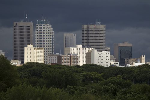 RUTH BONNEVILLE / WINNIPEG FREE PRESS  A burst of sunshine lights the skyline of Winnipeg as rises out of  a carpet of green trees with a dark backdrop Thursday  afternoon.    Aug 04, 2016