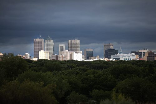 RUTH BONNEVILLE / WINNIPEG FREE PRESS  A burst of sunshine lights the skyline of Winnipeg as rises out of  a carpet of green trees with a dark backdrop Thursday  afternoon.    Aug 04, 2016