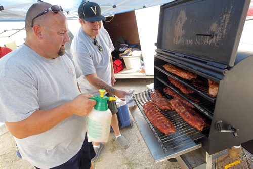BORIS MINKEVICH / WINNIPEG FREE PRESS The BBQ and Blues Festival kicks off Friday evening. They start setting up today and the cook off is tomorrow (Saturday) The event is in and around the Burton Cummings Theatre with entertainment too. In this photo Kevin Overholt, left, sprays some special juice on some ribs while his assistant Jamie Longe, right/behind looks on. Overholt, left, is the Pit Boss and is from Shawnee, Kansas. Longe, right/behind, is from Winnipeg. The team is based out of Winnipeg. They are cooking the ribs for a special family and friends meal this evening. The competition ribs get cooked tomorrow. August 19, 2016