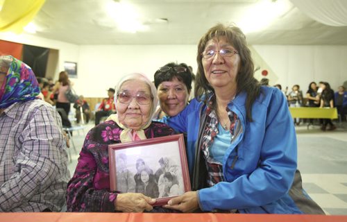 RUTH BONNEVILLE  / WINNIPEG FREE PRESS  Survivors Nancy Powderhorn gives her mom Rubina Duck a hug (with her sister behind her also in photo) in Tadoule Lake hall after minister Carolyn Bennett made formal apology for the forced relocation by the government of the Dene people, Tuesday. They hold a family photo of Nancy (centre) her mom (right) and sisters taken while they lived in Little Duck Lake 60 years ago prior to the forced move that destroyed their lives.   See Alex Paul story.    Aug 16 / 2016