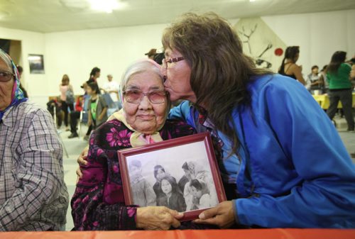RUTH BONNEVILLE  / WINNIPEG FREE PRESS  Survivors Nancy Powderhorn gives her mom Rubina Duck a hug in Tadoule Lake hall after minister Carolyn Bennett made formal apology for the forced relocation by the government of the Dene people, Tuesday. They hold a family photo of Nancy (centre) her mom (right) and sisters taken while they lived in Little Duck Lake 60 years ago prior to the forced move that destroyed their lives.   See Alex Paul story.    Aug 16 / 2016