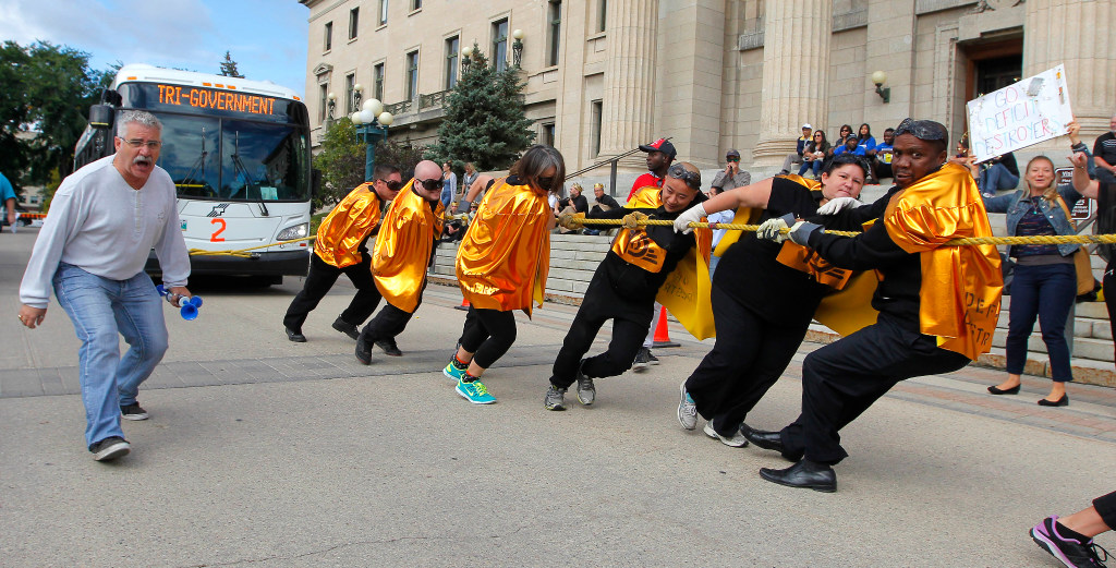 BORIS MINKEVICH / WINNIPEG FREE PRESS
STANDUP - 2016 Tri-Government Bus Pull at the Manitoba Legislative Building Grounds - South Plaza.The Challenge has been issued to all participating federal, provincial and municipal departments to enter teams in the 2016 Tri-Government 8th Annual Bus Pull to show their pride, have fun, beat last year's time and help raise awareness for the Government All Charities and United Way campaigns. 

In this photo the team from Manitoba government Department of Families called "Deficit Destroyers" make an effort to win over a team from Agriculture and Agri-Food Canada called "A Cruel Accounting" (not seen in the photo). This was heat #6 of 26. Left to right is City of Winnipeg employee and event volunteer Fernando Requeima (screaming cheering the pullers), Team Deficit Destroyers pulling Bus 2 - Kris Piche, Dan Fingler, Linda English, Gary Ma, Charissa McIntosh, and Sylvester Aghidi. Sept. 9, 2016