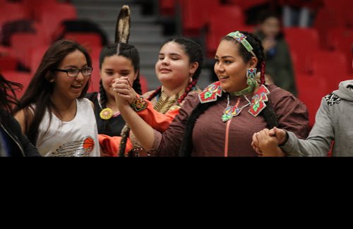 
RUTH BONNEVILLE / WINNIPEG FREE PRESS

Jingle dress dancers Autumn Monkman (right) , Iroc Levasseur (centre) and Ainsley Clarke lead members of the audience watching the Canada West Basketball Tournament at the U of W into a round dance during halftime Thursday evening.  The women and mens U of W Wesman teams were playing the Brandon University Bobcats.  
Standup 2
November 24, 2016