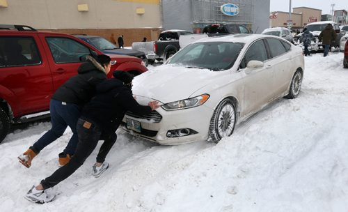 WAYNE GLOWACKI / WINNIPEG FREE PRESS

Yi Fan Yang and Nelson Tam,right, lend a hand to a Boxing Day shopper stuck in the snow in the strip mall parking lot along St. James St. Monday morning.  Dec.26 2016