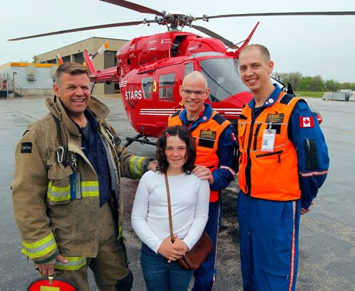 BORIS MINKEVICH / WINNIPEG FREE PRESS
Charity Edwards, in white shirt,  was transported by STARS in late 2015 after being struck by a vehicle while riding her bicycle in the Grunthal area. She sustained critical life-threatening injuries. She was at the STARS base at the airport today meeting some of the people who were involved in her rescue. From left, Grunthal Volunteer Fire Dept. Capt. Carl Reimer, Charity Edwards, STARS Medical Director Doug Martin, and STARS pilot David Harris. They posed for a group shot in front of the chopper.. RANDY TURNER STORY. May 16, 2017