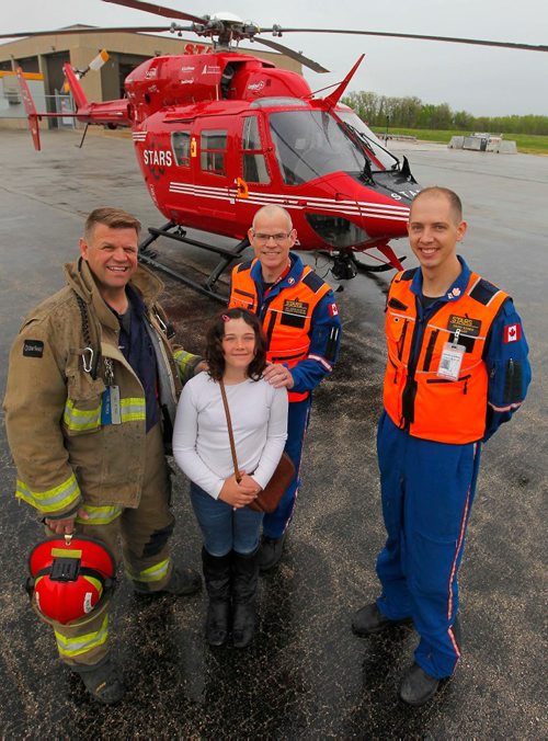 BORIS MINKEVICH / WINNIPEG FREE PRESS
Charity Edwards, in white shirt,  was transported by STARS in late 2015 after being struck by a vehicle while riding her bicycle in the Grunthal area. She sustained critical life-threatening injuries. She was at the STARS base at the airport today meeting some of the people who were involved in her rescue. From left, Grunthal Volunteer Fire Dept. Capt. Carl Reimer, Charity Edwards, STARS Medical Director Doug Martin, and STARS pilot David Harris. They posed for a group shot in front of the chopper.. RANDY TURNER STORY. May 16, 2017