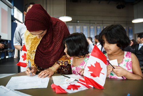 MIKE DEAL / WINNIPEG FREE PRESS
Mudasra Kashif signs some papers while her five-year-old twin daughters, Amna and Tehreen watch, during a special citizenship ceremony in celebration of Canada's 150th birthday, at the Investors Group Field.
170628 - Wednesday, June 28, 2017.