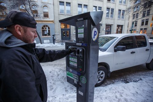 MIKE DEAL / WINNIPEG FREE PRESS
Michael Matsyk plugs a meter with change Tuesday afternoon in the Exchange District.
Some parking meters in the Exchange area have new stickers on them explaining the hourly rates. The two free hours on Saturday stickers are still there as well.
180102 - Tuesday, January 02, 2018.