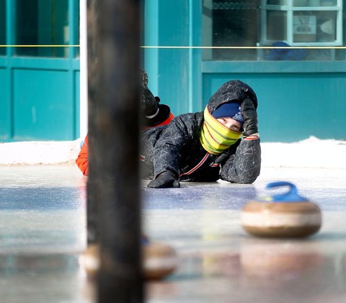 PHIL HOSSACK / Winnipeg Free Press - Stand-Up - 9 Yr old Nathan Kendall peers out from underneath his winter geat watching his shot on the Crokinole/curling ice at the Forks Saturday afternoon. He and his brother Andrew were warming up for their match in the weekend tournament. -  February 10, 2018