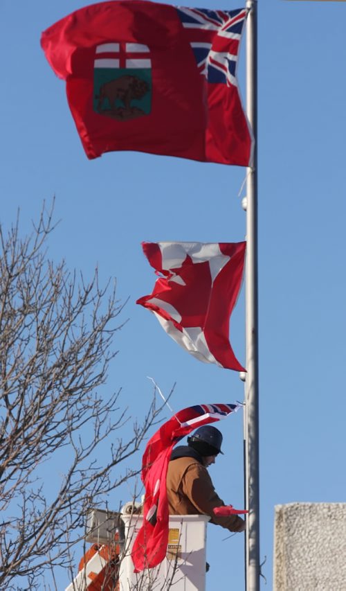 Brandon Sun James Wall installs new flags to replace those torn by the wind on the Brandon Sun building, Thursday morning on Rosser Avenue.   (Colin Corneau/Brandon Sun)