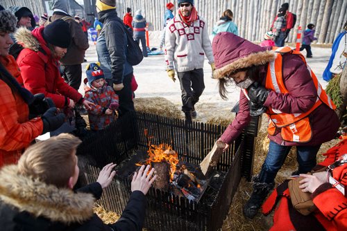 MIKE DEAL / WINNIPEG FREE PRESS
A volunteer places a log onto a camp fire as people stop by to warm up for a few minutes during the last weekend at the Festival du Voyageur in Fort Gibraltar.
180224 - Saturday, February 24, 2018.