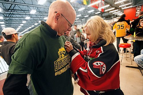 PHIL HOSSACK / WINNIPEG FREE PRESS -  Parents of Virden Oil Capitols Riley McVeigh, Shelly McVeigh pins a green ribbon on her husband Cam's t-shirt in respect for the Humbolt Bronco's. They're in the concourse at the Virden Tundra Oil Gas Place  Thursday. In town from Calgary to support their son they plan on carrying on to Steinbach for the third game Saturday in the final MJHL series. Melissa Martin story.- April 12, 2018