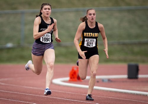 ANDREW RYAN / WINNIPEG FREE PRESS Zoie Forgue, runs alongside Daniele Dyck, left, a student from Vincent Massey High School who won the varsity 100 metre sprint during the MHSAA track and field event on June 8, 2018.