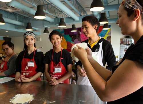 ANDREW RYAN / WINNIPEG FREE PRESS Kayla Umali, left, Erika Yazon, and Winzy Hinsunarin watch Camille Metcalf demonstrate how to toss pizza dough at the Food Justice Club on June 13, 2018. The after school club at the NorWest Co-op Community Health is lead by chef Metcalf.