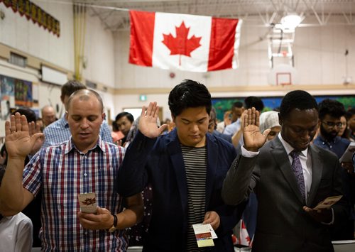 ANDREW RYAN / WINNIPEG FREE PRESS Immigration, Refugees and Citizenship Canada inducted 38 new citizens in a special ceremony held at École Luxton School. Originally from the Philippines Mark Jovero, centre, is pictured raising his hand as he takes the oath of citizenship.