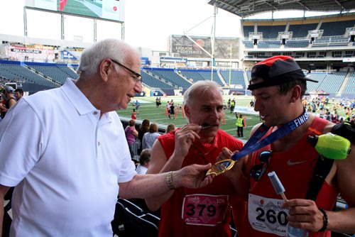 MAGGIE MACINTOSH / WINNIPEG FREE PRESS
Arie Bronk, 81, touches his grandson Dylan Bronk's Manitoba Marathon medal Sunday as Bob Bronk, 58, bites his 10 km medal. June 17, 2018
