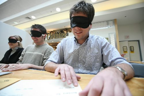 Brandon Sun 16012009 Grant Hamilton (R) with the Brandon Sun takes part in the CNIB Braille Identification Challenge alongside other members of the media in front of the Coles bookstore in the Shoppers Mall on Friday morning. Participants were challenged to identify the phrase Braille 200 on a sheet of braille while blindfolded. The event was one of many worldwide marking the 200th anniversary of Louis Braille's birth. (Tim Smith/Brandon Sun)