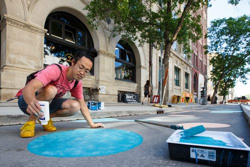 MIKE DEAL / WINNIPEG FREE PRESS
Artist Takashi Iwasaki paints designs in a stretch of the new protected bike lane on McDermot Wednesday afternoon.
180627 - Wednesday, June 27, 2018.