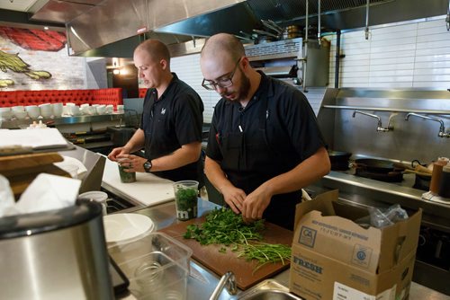 MIKE DEAL / WINNIPEG FREE PRESS
The Merchant Kitchen restaurant at 314 Donald Street.
Opening line cook Ian Shapira (right) prepares cilantro for the day while executive chef Jesse Friesen (left) starts organizing for the opening in an hour.
The kitchen prepares food from their updated menu for a social media promotion including a sneak peak of their burger week creation which will debut at the beginning of September.
180713 - Friday, July 13, 2018.
24hourproject