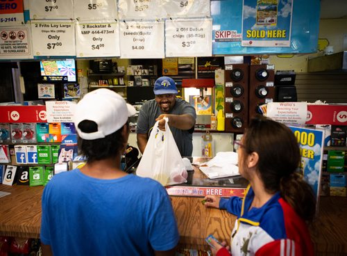 ANDREW RYAN / WINNIPEG FREE PRESS Walia store clerk Tewodros Tadesse hands a customer a hoagie sandwich around 4:00 a.m. on Friday July 13, 2018.The customer, a roofer, was picking up his day's food before heading to work in Winnipeg. He's pictured with Shannon Fawcett. 24hourproject