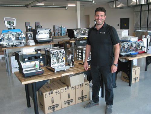 Canstar Community News July 18, 2018 = Marco De Luca stands next to some of the expresso and cappucino machines that the family business stocks. Their new location at 66 Siuth Landing in the RM of Macdonald will include an area focussing on the coffee brewing equipment and the coffee varieties and blends that Marco's father Peter roasts. (ANDREA GEARY/CANSTAR COMMUNITY NEWS)