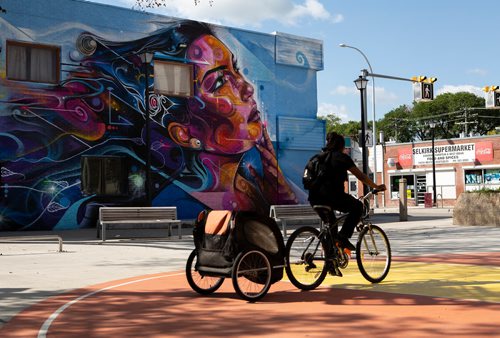ANDREW RYAN / WINNIPEG FREE PRES A woman rides her bike past the recently unveiled mural painted onto the side of The Ndinawe Youth Resource Centre by UK based artist Mr Cenz on July 26, 2018. The mural was commissioned by  the Graffiti Gallery and was gifted to the centre in honour of the community of families and survivors of Missing and Murdered Indigenous Women and Girls and to Ndinawemaaganag Endaawaad Inc. as a thank you for the work that they do in relation to the cause.