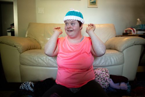 ANDREW RYAN / WINNIPEG FREE PRESS Solveig Meinhardt tries on one of her baby-sized hats. Meinhardt lives with Down syndrome and is donating her hand made hats to Koats for Kids. The 16-year-old learned to knit in November of 2017 and has knitted nearly 190 hats since then. She in pictured with about 75 of her hats on the family's living room floor on August 1, 2018.
