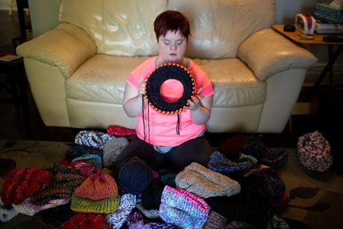 ANDREW RYAN / WINNIPEG FREE PRESS Solveig Meinhardt works with her loom in her family room on August 1, 2018. Meinhardt lives with Down syndrome and donating her knitted hats to Koats for Kids. The 16-year-old learned to knit in November of 2017 and has knitted nearly 190 hats since then. She in pictured with about 75 of her hats on the family's living room floor on August 1, 2018.