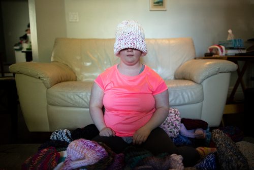 ANDREW RYAN / WINNIPEG FREE PRESS Solveig Meinhardt tries on one of her hand knitted hats. Meinhardt lives with Down syndrome and is knitting hats for Koats for Kids. The 16-year-old learned to knit in November of 2017 and has knitted nearly 190 hats since then. She in pictured with about 75 of her hats on the family's living room floor on August 1, 2018.