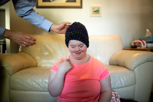 ANDREW RYAN / WINNIPEG FREE PRESS Solveig Meinhardt tries on one of her hand knitted hats. Meinhardt lives with Down syndrome and is donating her hats to Koats for Kids. The 16-year-old learned to knit in November of 2017 and has knitted nearly 190 hats since then. She in pictured with about 75 of her hats on the family's living room floor on August 1, 2018.