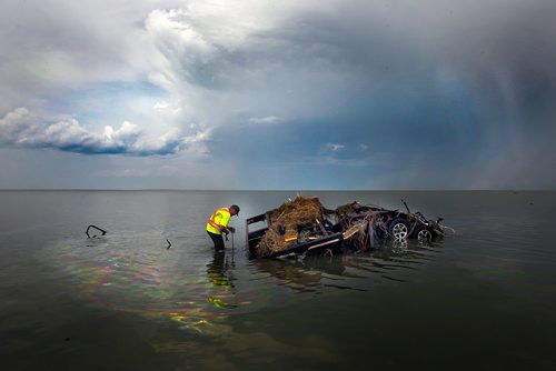 PHIL HOSSACK / WINNIPEG FREE PRESS -   Surrounded by an oily sheen while a squall blows across lake Manitoba behind him, Daniel Cottyn attaches a tow line to the wreckage of a camper in Lake Manitoba at the Margaret Bruce Beach and campground Tuesday. A tornado ripped through the Alonsa Manitoba area Friday. See story. - August 7, 2018