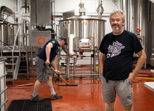 ANDREW RYAN / WINNIPEG FREE PRESS Paul Clerkin of Stone Angel poses for a portrait, while co-owner Paul McMullan prepares to brew in the company's in-house brewery. Clerkin is part of the collective of brewers operating out of the same facility in the belief that strength in numbers will help the brewers' success against international beer conglomerates. Shot on August 10, 2018.