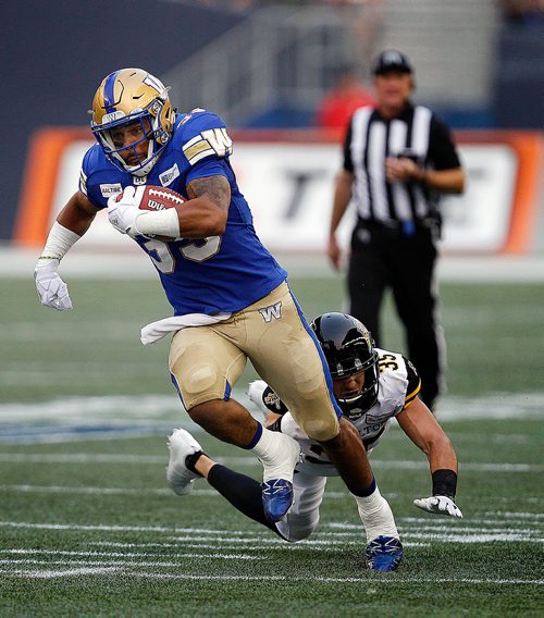 PHIL HOSSACK / WINNIPEG FREE PRESS - Winnipeg Blue Bomber #33 Andrew Harris takes off past a flying dive from Hamilton Ti-Cat # 35 Mike Daly Friday night at Investor's Group Stadium in Winnipeg. See story. - August 10, 2018