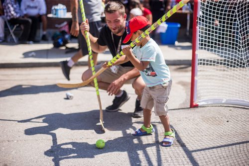 MIKAELA MACKENZIE / WINNIPEG FREE PRESS
Carter Bergen helps Jace McKay, three, play a pickup street hockey game hosted by the Main Street Project on Martha Street in Winnipeg on Wednesday, Aug. 15, 2018. 
Winnipeg Free Press 2018.