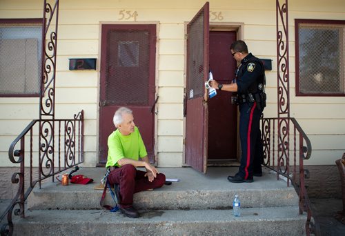 ANDREW RYAN / WINNIPEG FREE PRESS Albert Collette, a resident of the William Whyte neighbourhood for eight years, sits as officer Martin Boileau knocks on his neighbour's door part of the Winnipeg Police's attempt to increase their positive presence in the city's north end neighbourhood on Manitoba Ave. on August 15, 2018.