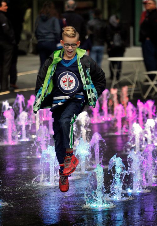 PHIL HOSSACK / WINNIPEG FREE PRESS -  With the compass rose Jet on his Jersey pointing True North, 7 yr old Draden Dueck dances in the "water feature" at the newly opened True North Square on his way to the Jets game with his parents Thursday. The Square was officially opened to the public for the first time this afternoon.  - Sept 27, 2018
