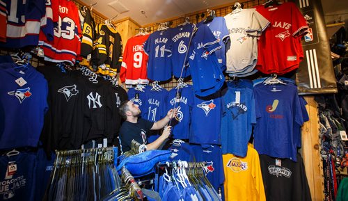 MIKE DEAL / WINNIPEG FREE PRESS
Employee Andre Vien takes down a Blue Jays jersey for a customer at Uptown Sports which is on the 2nd level of Portage Place Shopping Centre and is celebrating its 15th anniversary in downtown Winnipeg.
181018 - Thursday, October 18, 2018.